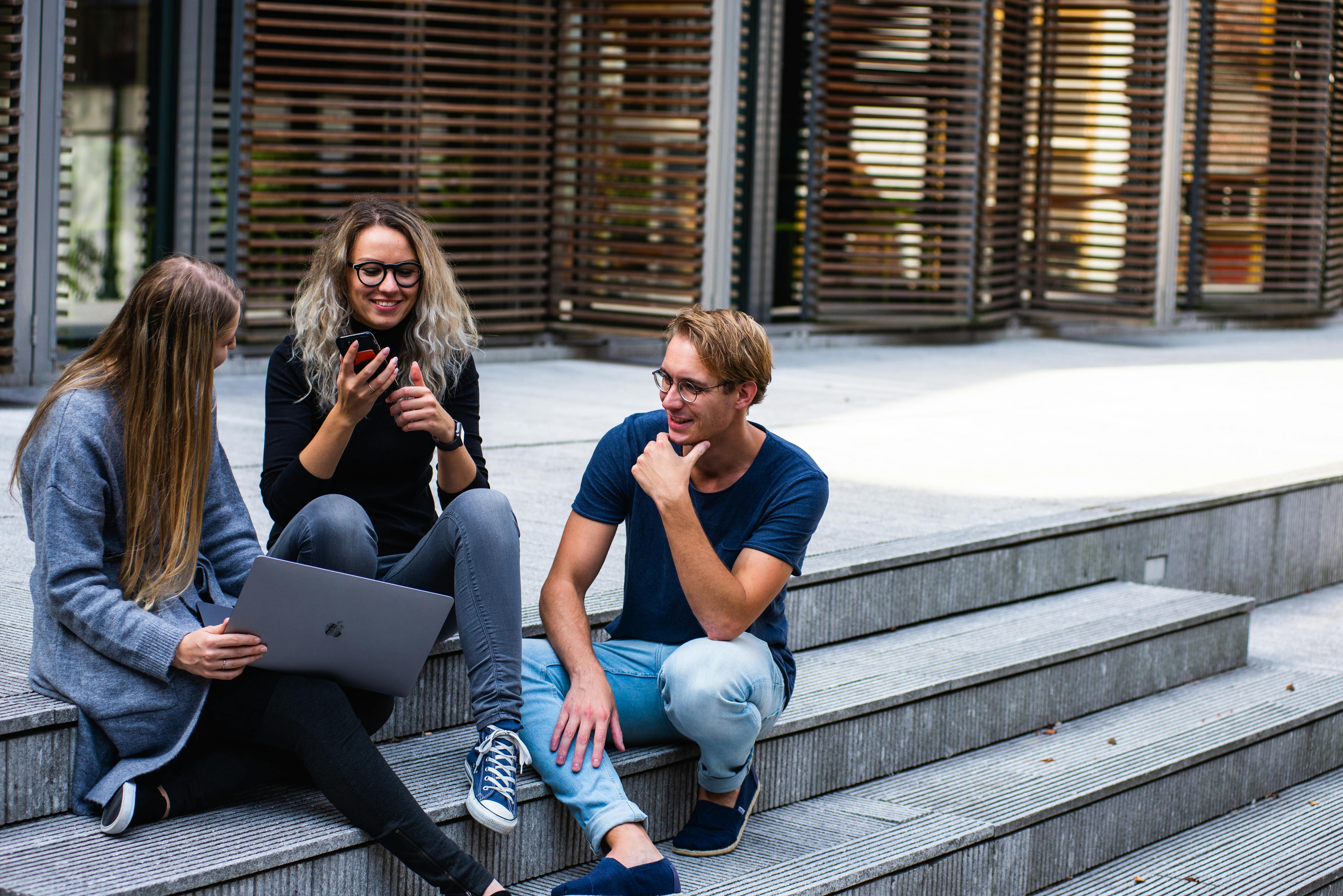 Three students are discussing together by sitting on the stairs.